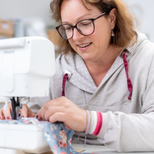 Anke Towfighi - Inhaberin von Anke's Nähbox sie sitzt gerade an einer Nähmaschine und näht ein stück Stoff zusammen